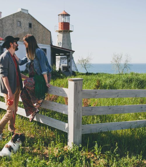 young stylish hipster couple in love walking with dog in countryside, summer style boho fashion